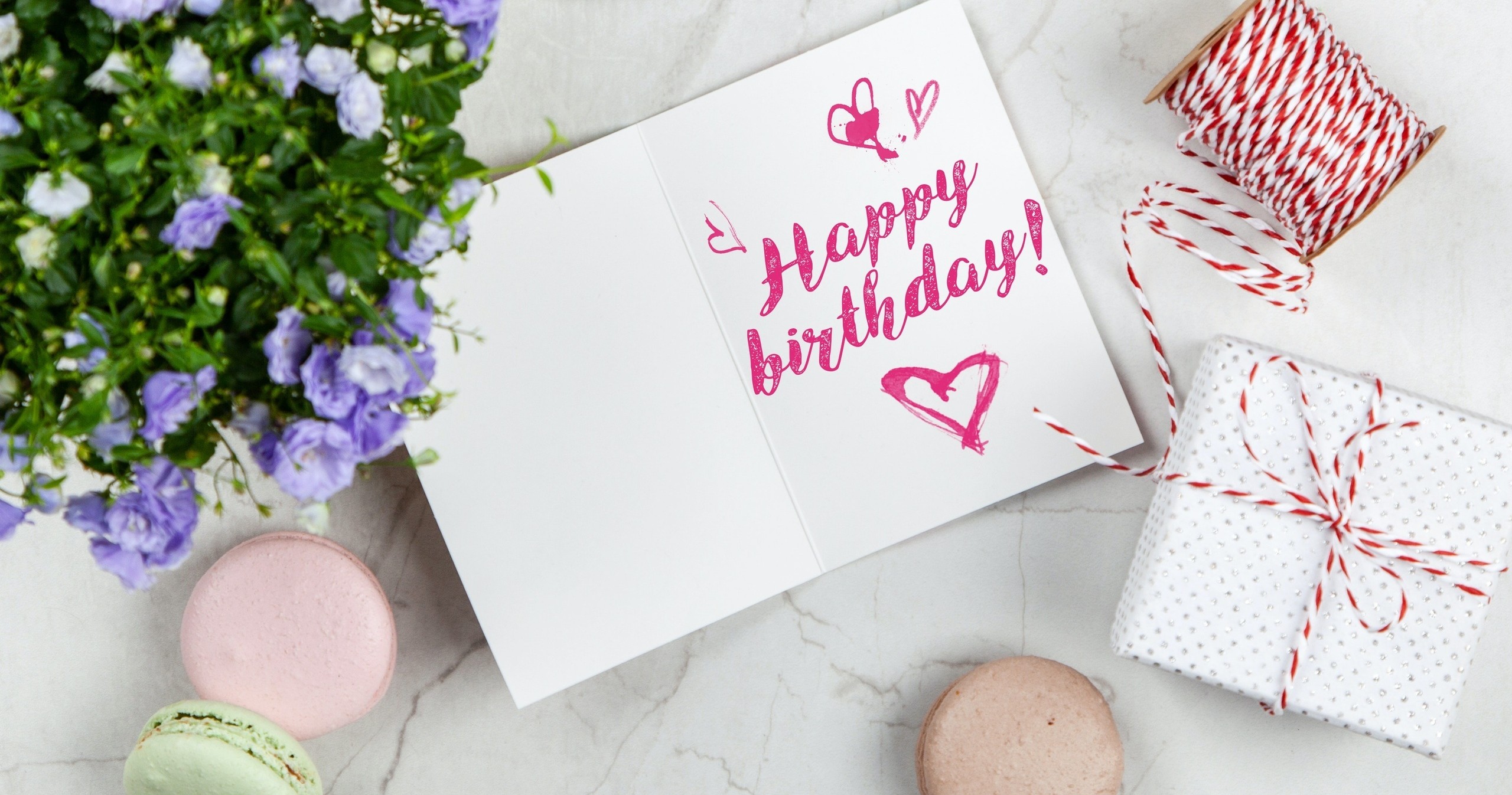 Birthday card with hearts, macarons, plant, and wrapped gift on marble surface.