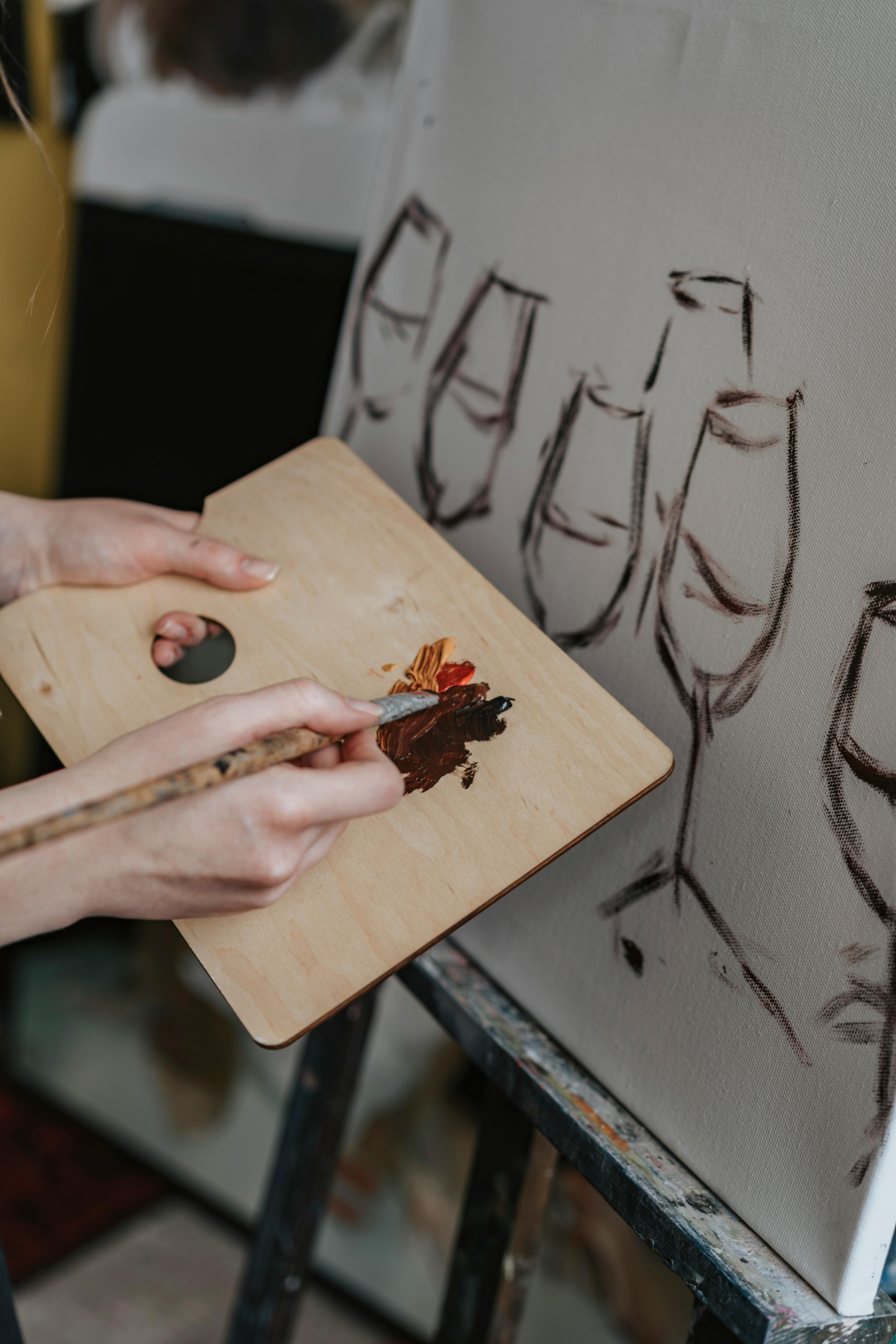 Person painting wine glasses on a canvas using a palette and brush.