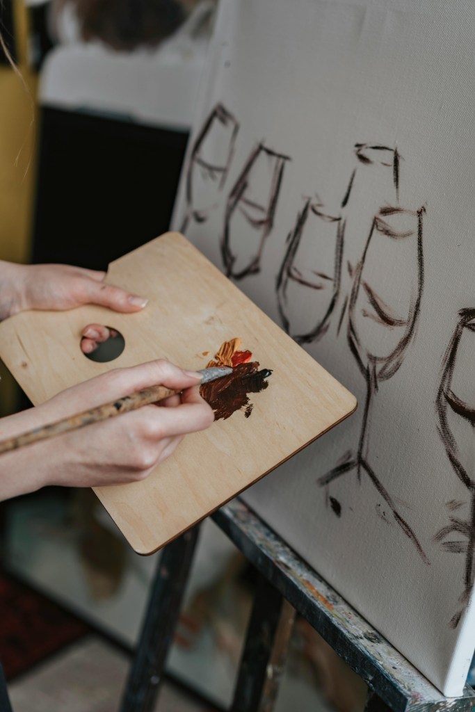 Person painting wine glasses on a canvas using a palette and brush.