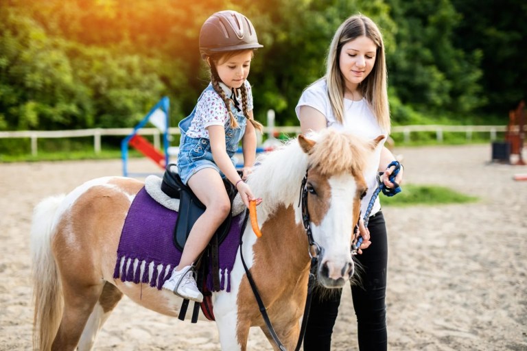 Girl riding a pony led by a woman in an outdoor setting.